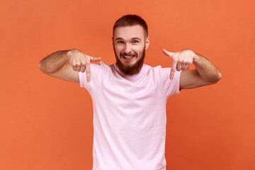 Cheerful satisfied man pointing fingers down, paying attention to advertising area, blogger...