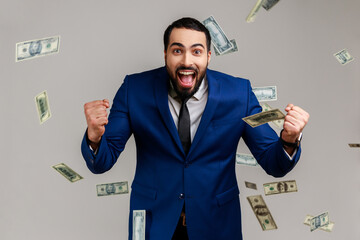 Excited bearded man standing under money with clenched fists and yelling happily, celebrating...