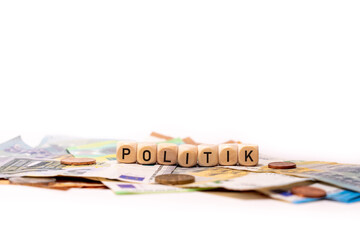 German word for Politics, POLITIK, spelled with wooden letters wooden cube on a plain white background with banknotes and coins, concept image