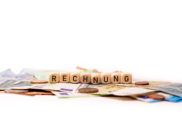 German word for invoice, RECHNUNG, spelled with wooden letters wooden cube on a plain white background with banknotes and coins, concept image