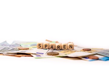 German word for saving, SPAREN, spelled with wooden letters wooden cube on a plain white background with banknotes and coins, concept image