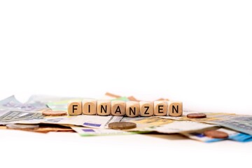 German word for finances, FINANZEN, spelled with wooden letters wooden cube on a plain white background with banknotes and coins, concept image