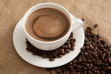 Cup with coffee and coffee beans and steam over cup on burlap background