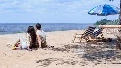 Young couple sitting near orange juice and deck chairs on beach