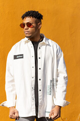 portrait of a black Latino man wearing sunglasses with clenched fists with angry gesture, yellow vertical background