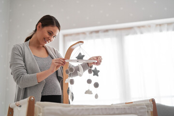 Caucasian pregnant woman installing a baby mobile toy over the baby's crib