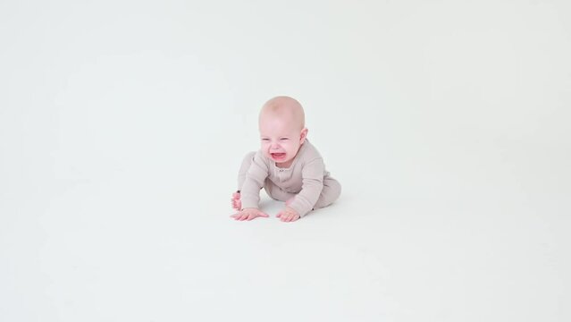baby girl in a baby bodysuit is sitting crying on a white background
