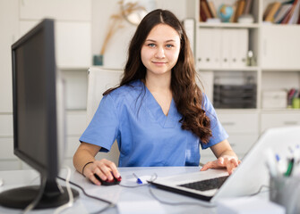 Portrait of female doctor who is working with laptop