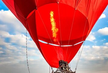 Filling a balloon with hot air from a burning gas burner against a blue sky with white clouds in summer