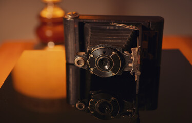 Vintage photo camera and its reflection on an interior deco setup with an old lamp in background.