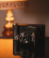 Vintage photo camera and its reflection on an interior deco setup with an old lamp in background.