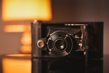 Fototapeta na wymiar Vintage photo camera and its reflection on an interior deco setup with an old lamp in background.