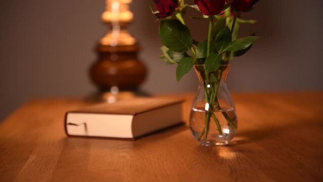 4k video with red roses flowers and a book in background. Mood photo with a vintage lamp and a wooden table. Interior deco ideas.