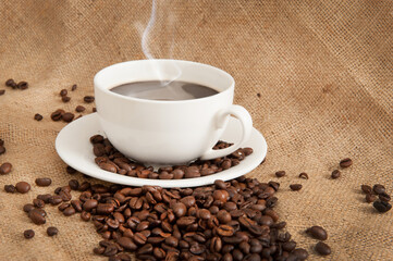 Cup with coffee and coffee beans and steam over cup on burlap background