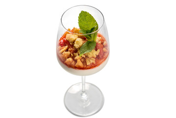 Panna cotta italian dessert with strawberry syrup and crumbled cake with mint leaves in glass goblet glass, top view, isolated on white