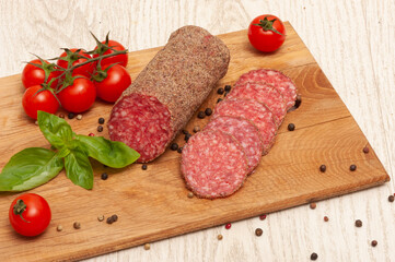 Sausage on a wooden board with cherry tomatoes and basil