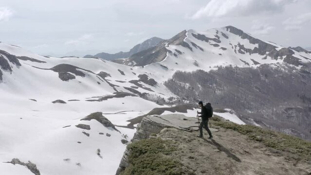Hiker reaching the top of mountain peak surrounded by mountains covered in snow