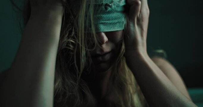 unhappy blind woman sits alone in a dark room with covered eyes, close