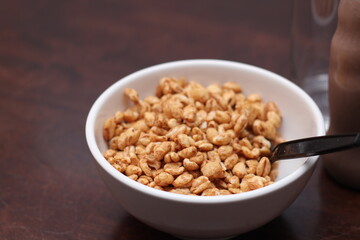 cereal in a white cup with chocolate milk in a ready-to-eat glass jar Served on a brown wooden table.