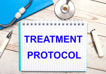 On a light wooden background there is a stethoscope, a blue notebook, a white pen and a sheet of paper with the text TREATMENT PROTOCOL. Medical concept