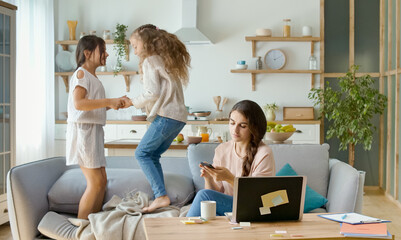 A Busy Mother Trying to Work Remotely at Home. On The Background Her Daughters are Running Around The Table, While Their Mother Working With a Laptop and Doing Business Conversation on the Phone.