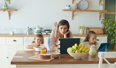 Lovely Mother to Take Care of Her Cute Daughters While Working With a Laptop at the Table and Doing Business Conversation on the Phone in the Kitchen. Mother is Working Remotely,