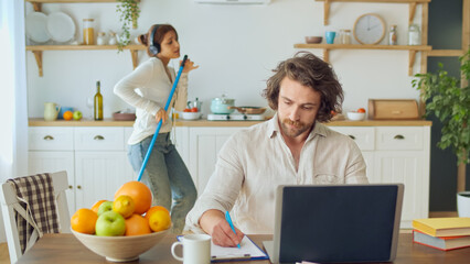 Attractive Man Trying to Work Remotely While His Wife With Headphones Dancing and Singing Karaoke...
