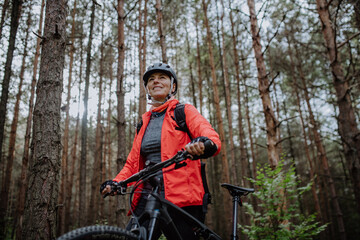 Fototapeta na wymiar Low angle view of senior woman biker walking and pushing bike outdoors in forest in autumn day.