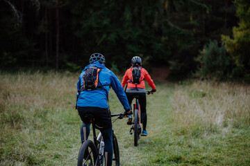 Fototapeta premium Rear view of active senior couple riding bikes outdoors in forest in autumn day.