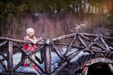 Baby in the winter forest. Girl on a wooden bridge. Baby in winter coat. Girl in early spring. Beautiful girl with long hair in a hat. Girl in a sweater. Girl in mittens