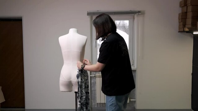 A seamstress woman measures a fabric billet of pants on a mannequin in an atelier