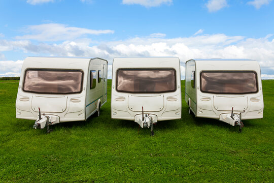 Caravan travel trailers used for outdoor camping which are parked up in a green grass campsite park field where a family can enjoy a fun vacation at their holiday travel destination, stock photo image