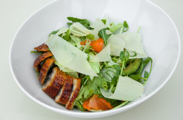 Salad on a white plate with green lettuce, herbs, parmesan cheese, tomatoes and baked meat fillet, healthy and proper nutrition, weight loss diet