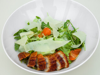 Salad on a white plate with green lettuce, herbs, parmesan cheese, tomatoes and baked meat fillet, healthy and proper nutrition, weight loss diet