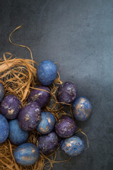 Easter card with a copy of the place for the text. Purple, blue and golden eggs on a dark background. The trend of 2022 purple shade is very peri. Natural dye karkade tea. Top view.