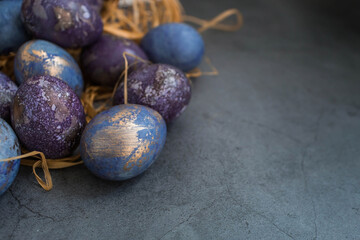 Easter card with a copy of the place for the text. Purple, blue and golden eggs on a dark background. The trend of 2022 purple shade is very peri. Natural dye karkade tea. Top view.