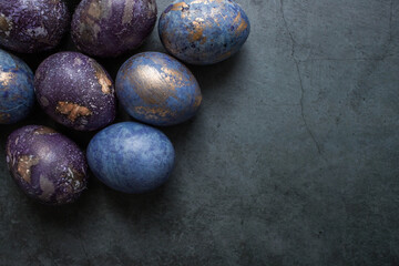Easter card with a copy of the place for the text. Purple, blue and golden eggs on a dark background. The trend of 2022 purple shade is very peri. Natural dye karkade tea. Top view.