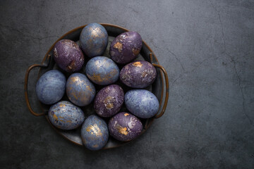 Easter card with a copy of the place for the text. Purple, blue and golden eggs in an iron plate on a dark background. The purple hue trend of 2022 is veryperi. Natural dye karkade tea. Top view.