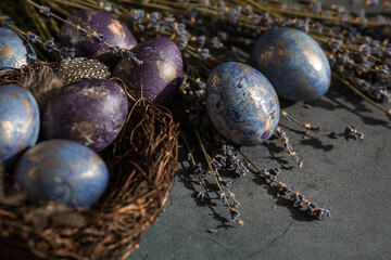 Easter card with a copy of the place for the text. Purple, blue and golden eggs with lavender on a dark background. The purple hue trend of 2022 is very relevant. Natural dye karkade tea. Top view.