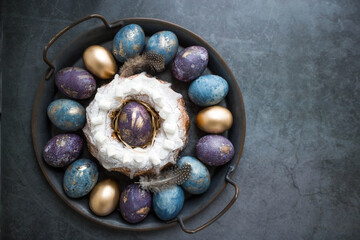 Easter card with a copy of the place for the text. Purple, blue and golden eggs with a cake on a dark background. The purple hue trend of 2022 is very peri. Natural dye karkade tea. Top view.