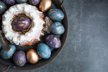 Easter card with a copy of the place for the text. Purple, blue and golden eggs with a cake on a dark background. The purple hue trend of 2022 is very peri. Natural dye karkade tea. Top view.
