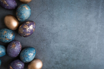 Easter card with a copy of the place for the text. Purple, blue and golden eggs on a dark background. The trend of 2022 purple shade is very peri. Natural dye karkade tea. Top view.