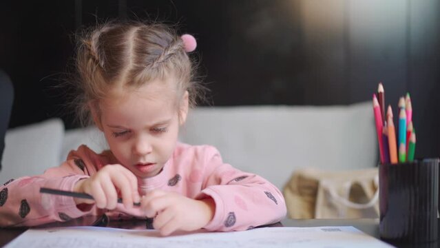 Child drawing sharpening pencils sitting on table middle shoot. Caucasian female little girl draws with colored pencils. Female child doing homework portrait shoot