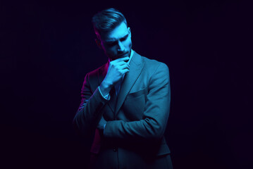 Young handsome model posing in a studio in a trendy neon light. Fashionable man in a stylish suit. Vibrant color. Bright colorful light effects. Disco style. Overlay. Gel filter. Supersaturated