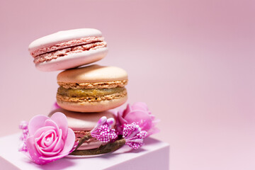Sweet dessert colored macaroons with a decor in the form of pink flowers and a pink podium on a light red background.