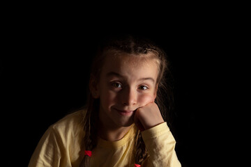 portrait of a girl on a dark background. the child smiles.