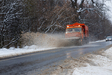 A large car with a plow clears the road from snow. Orange cargo special equipment is struggling...