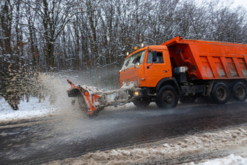 A large car with a plow clears the road from snow. Orange cargo special equipment is struggling...