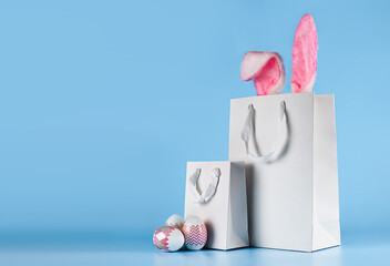 Banner on a blue background. The concept of online shopping for Easter, purchases and sale for the holiday. Gift bag with bunny ears and Easter eggs