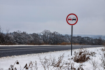 Snowy road with traffic sign Overtaking prohibited. Road in the countryside